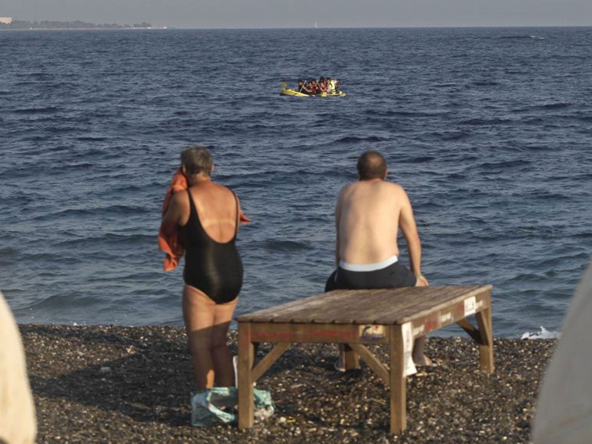 Bathers watch Pakistani migrants as they paddle a dinghy trying to disembark on the coast of Kos August 2015 (EPA)