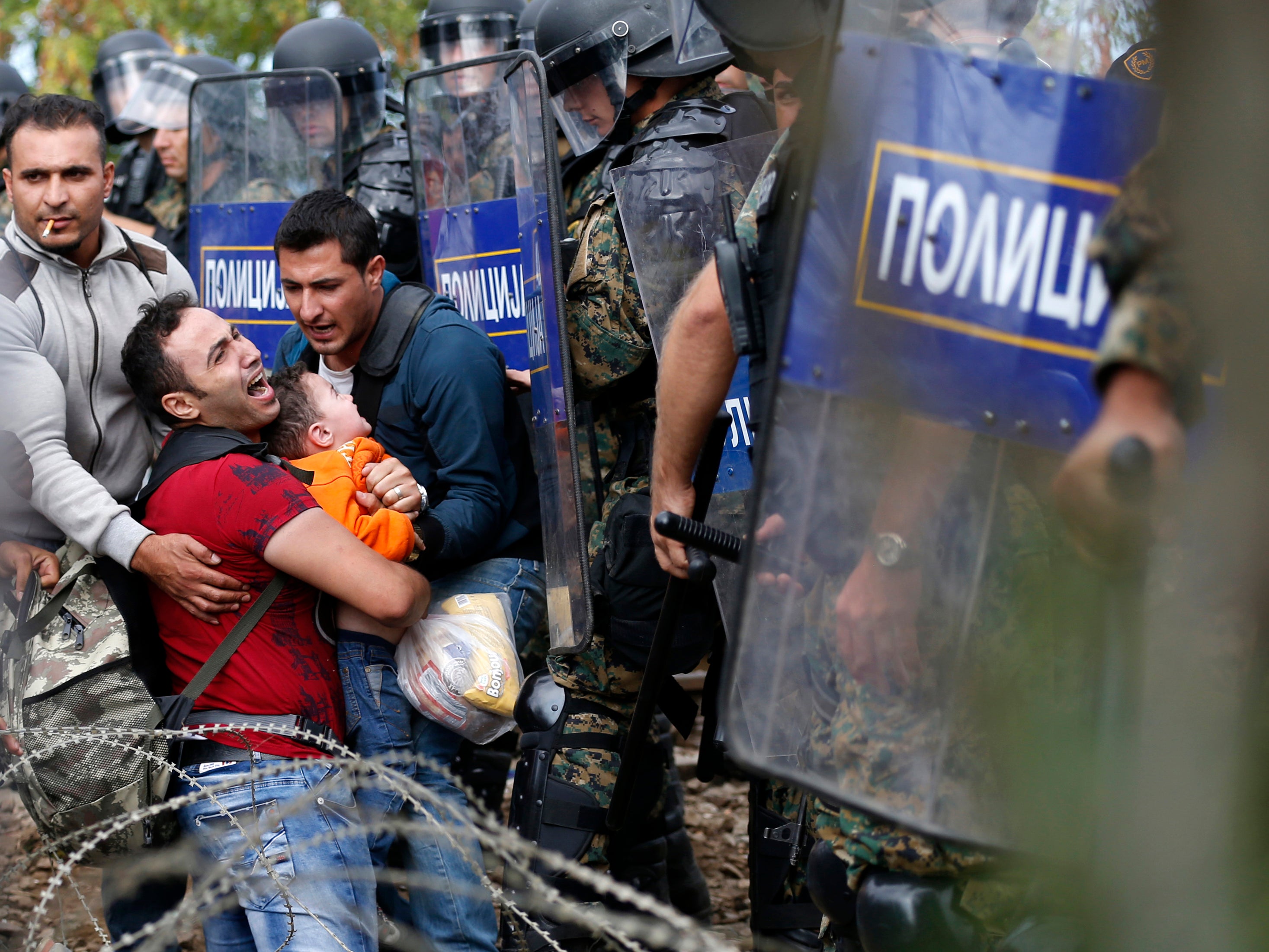 Migrant men help a fellow migrant man holding a boy as they are stuck between Macedonian riot police officers and migrants during a clash near the border train station of Idomeni,