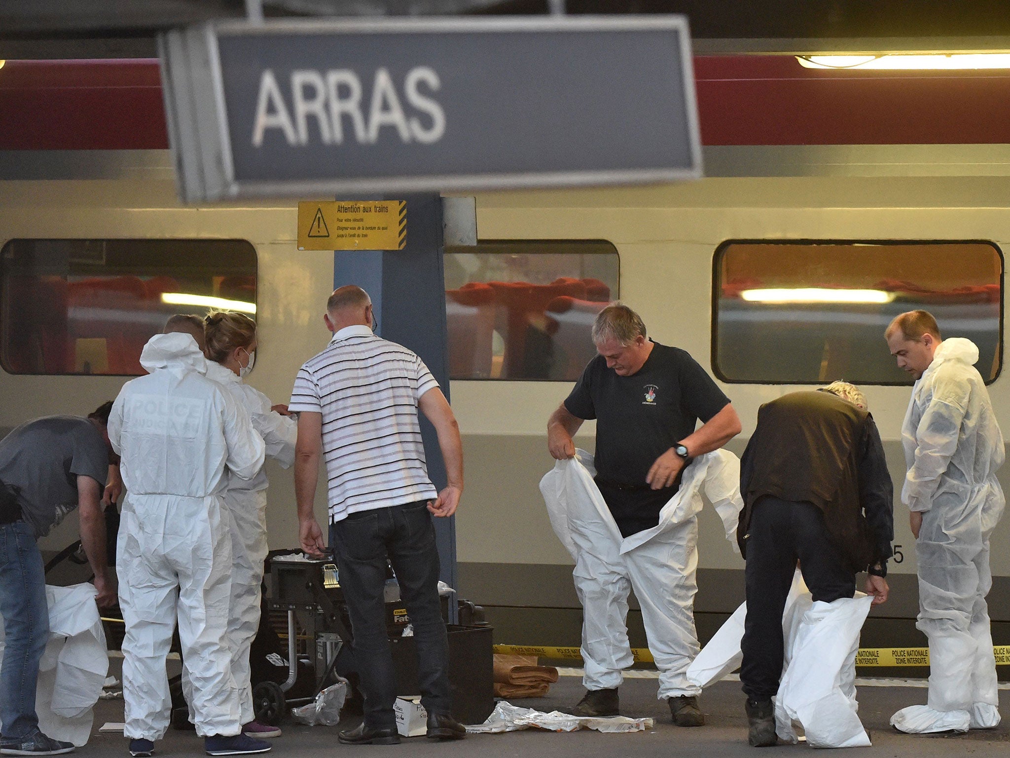 Criminal and forensic investigators put on protective suits on a platform next to a train at the train station in Arras