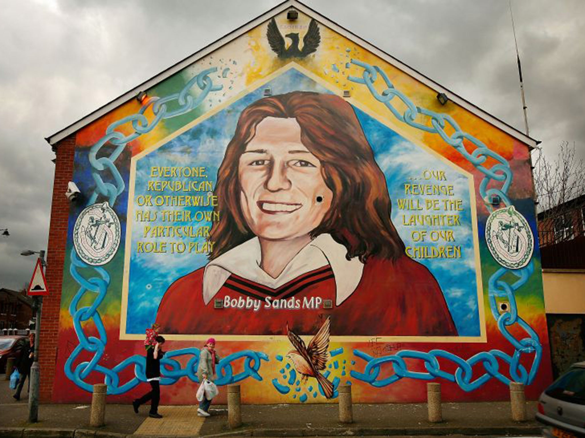 A couple walk past a mural depicting Bobby Sands in the Falls Road