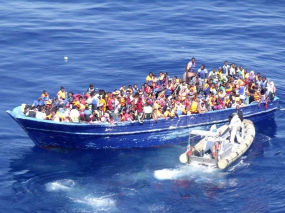 An Italian navy dinghy approaches a crowded migrant boat in the Mediterranean
