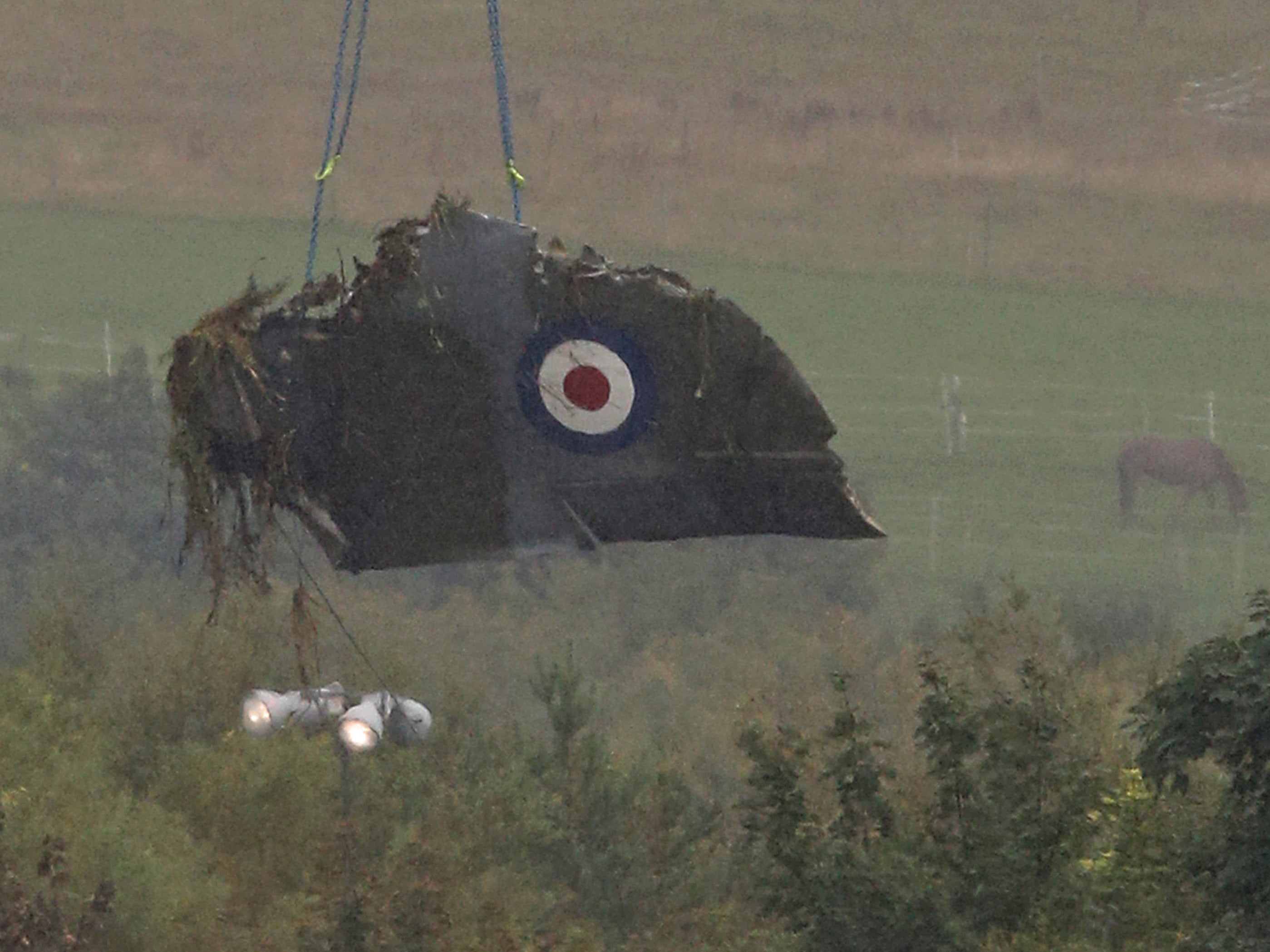 The damaged remains of part of the wing of a Hawker Hunter fighter jet are lifted away from the scene by crane