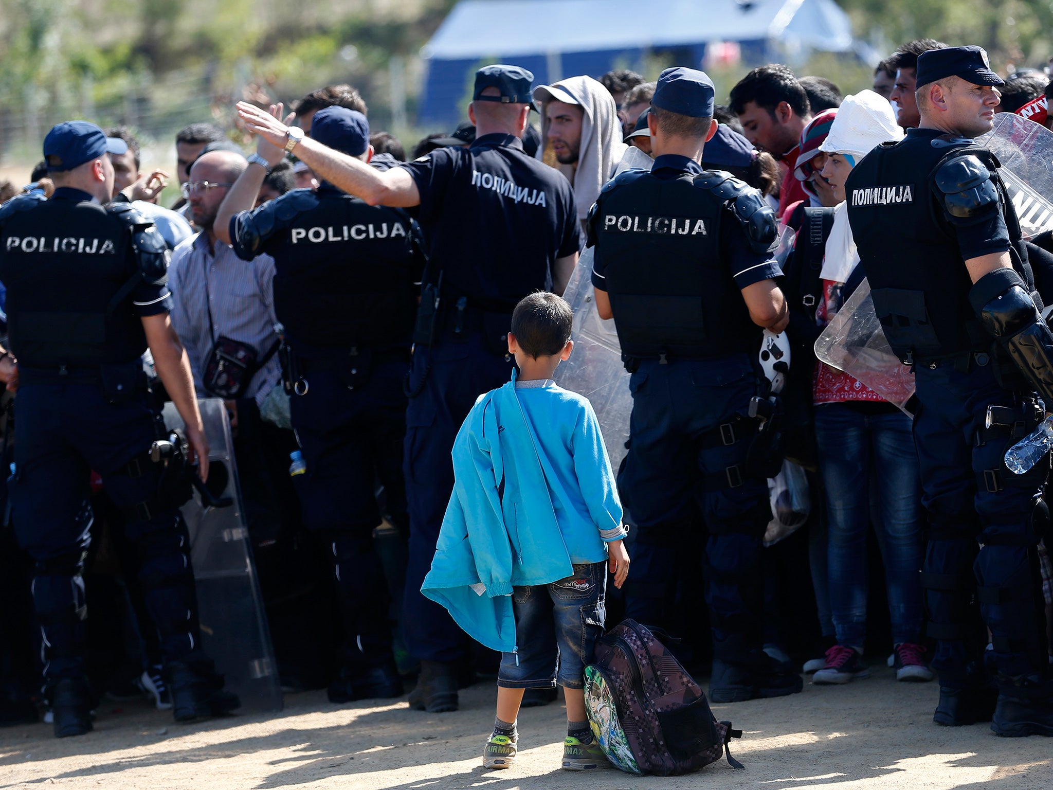 Serbian police officers watch a crowd of migrants as they cross from Macedonia, in the village of Miratovac
