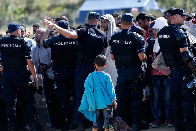 Serbian police officers watch a crowd of migrants as they cross from Macedonia, in the village of Miratovac 