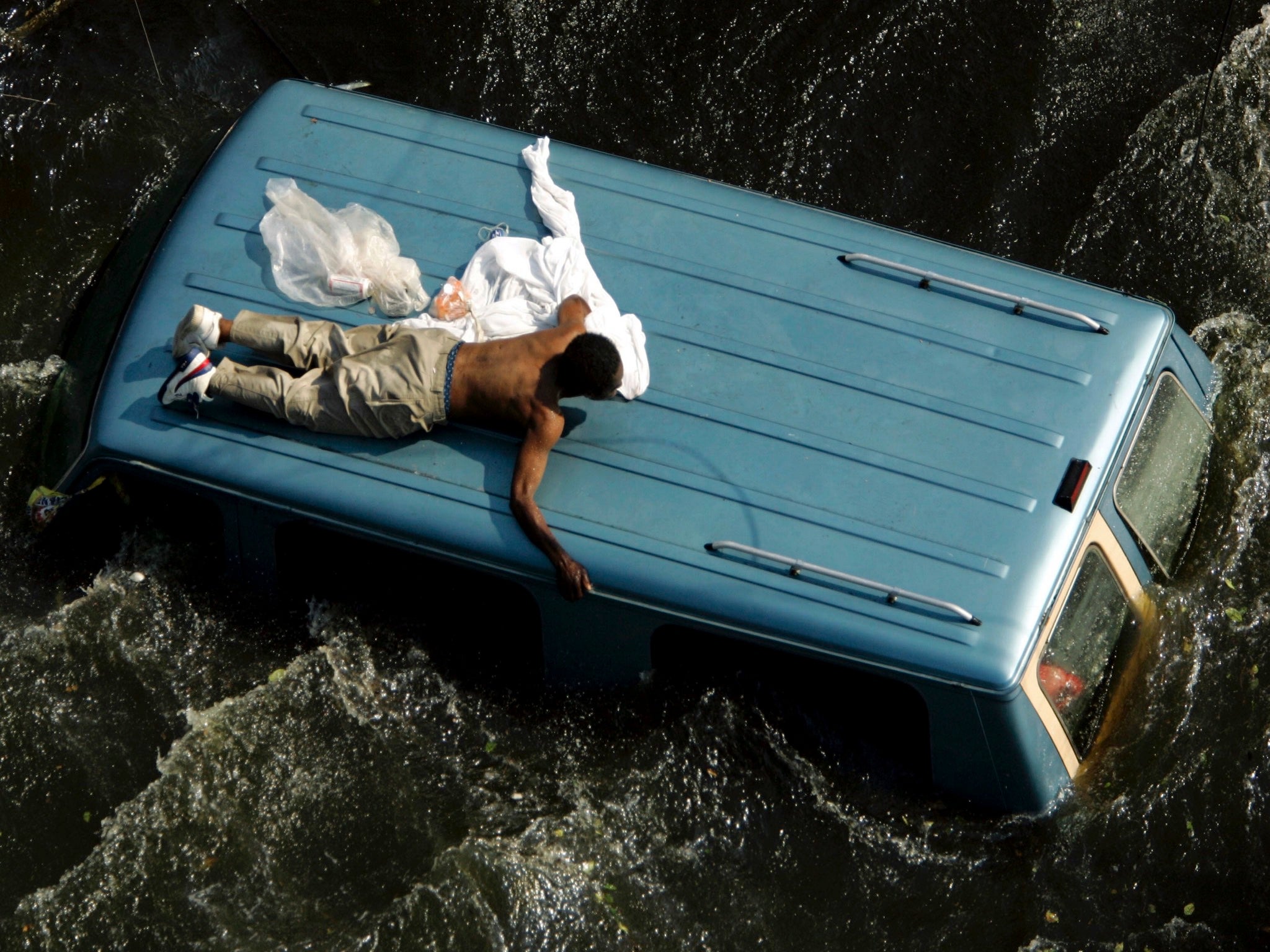 A man clings to a vehicle before being rescued by US Coast Guard after Katrina struck