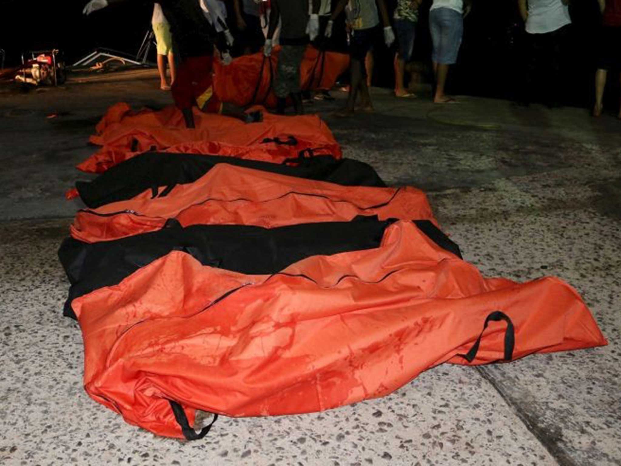 Body bags containing some of the people killed after two smugglers' boats capsized are brought ashore