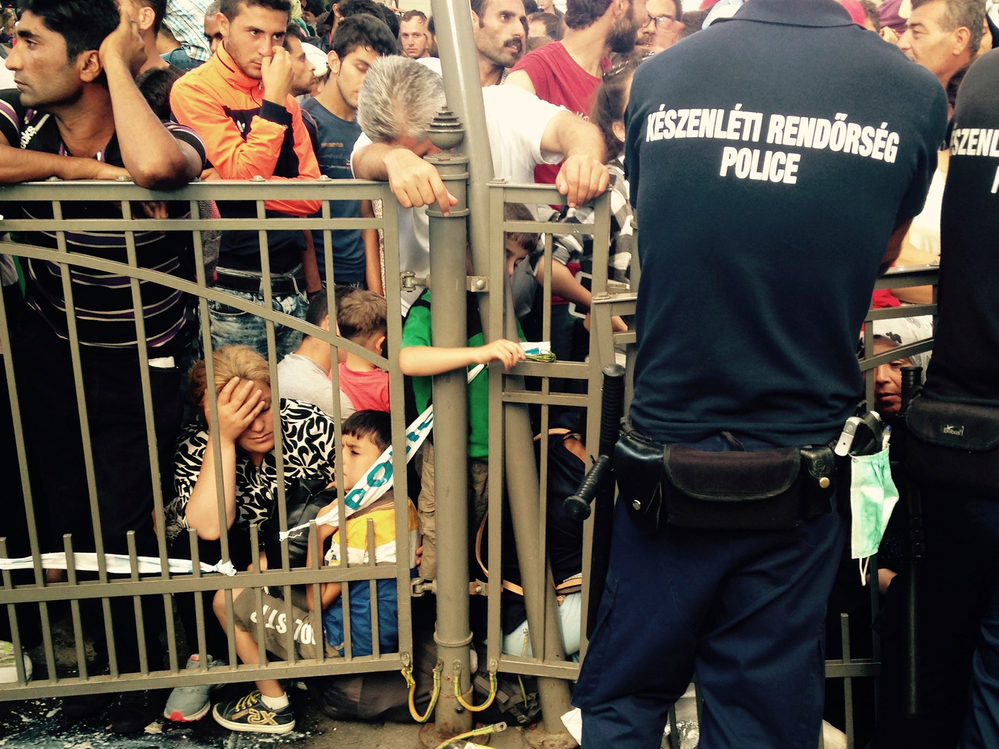 Migrants wait behind a fence guarded by police as the Keleti train terminal in Budapest