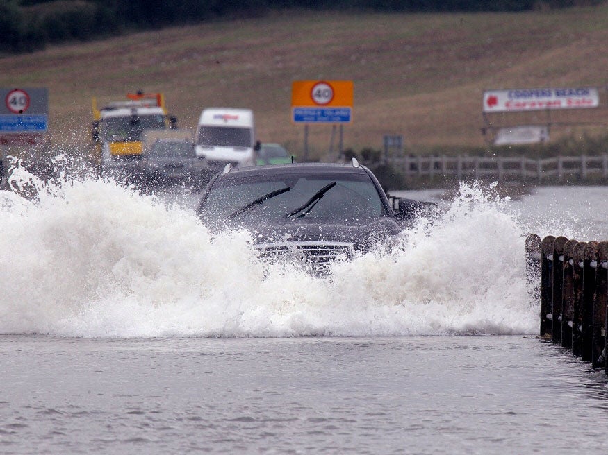 Motorist drives through a high tide on road linking Mersea Island, Essex