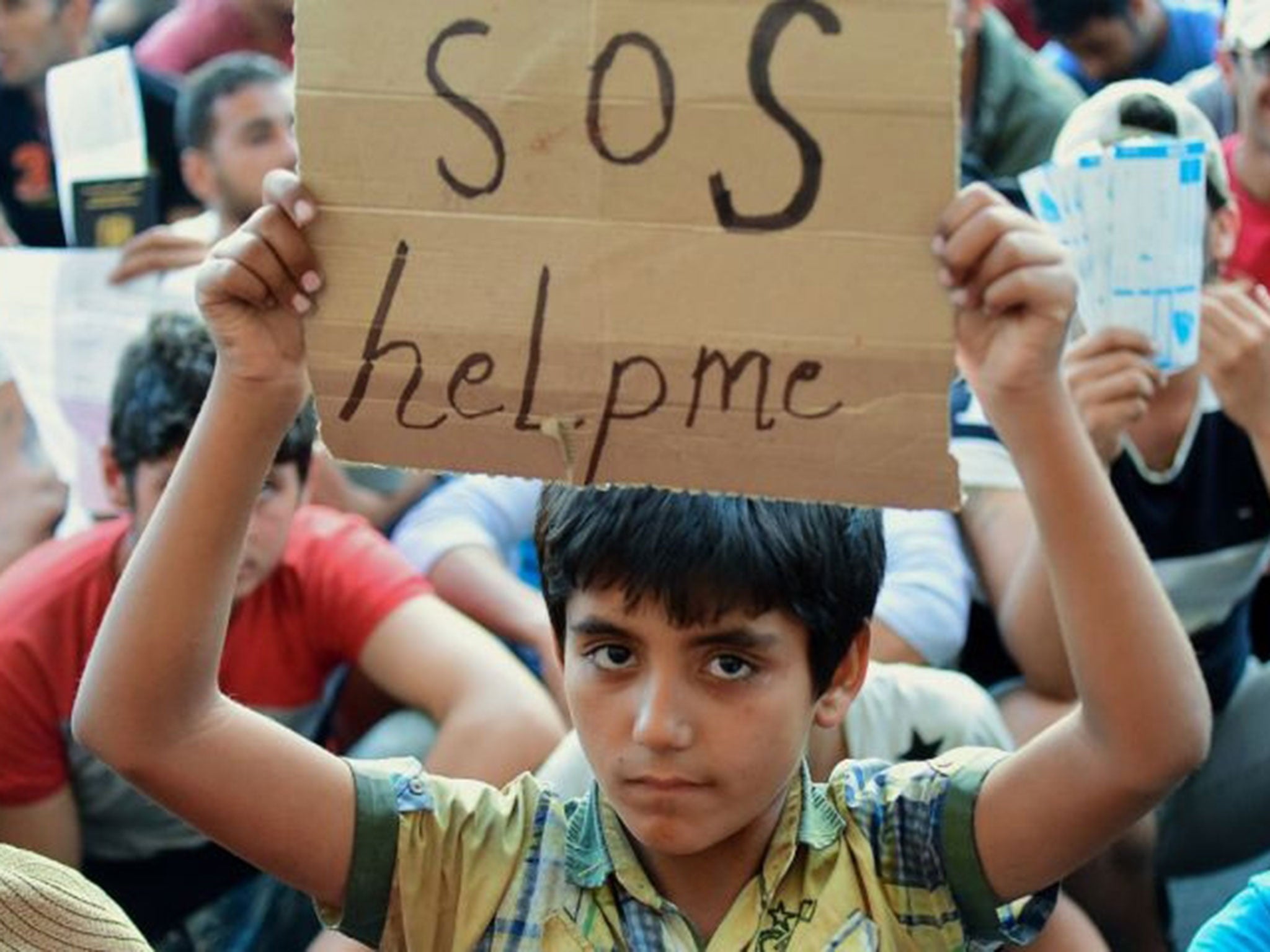A boy holds a sign reading 'SOS help me' as he sits with other migrants in front of the Keleti railway station in Budapest