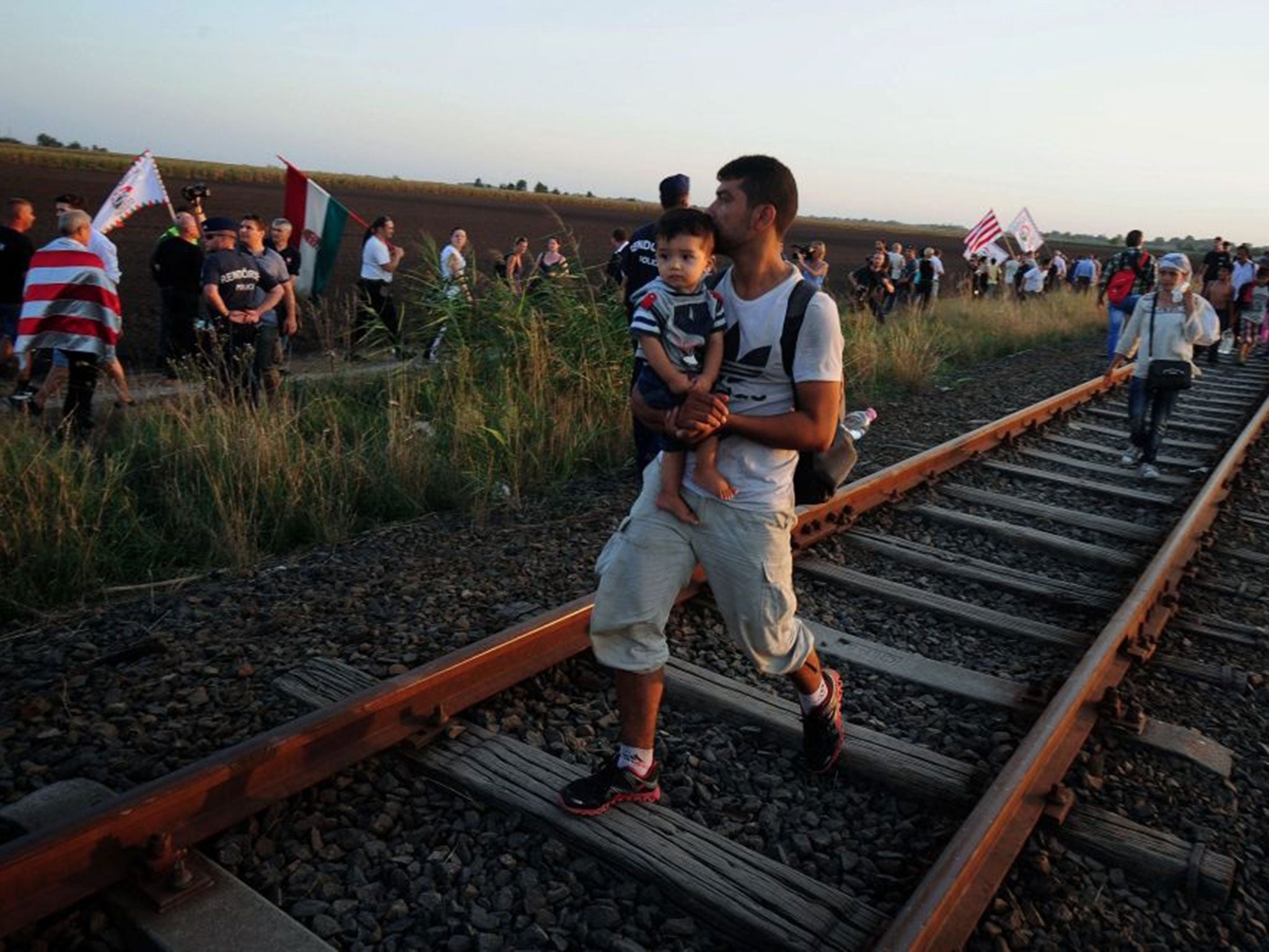 Migrants (R) arrive to Hungary walking between railways while crossing the Serbian border near Roszke village, southern Hungary, on September 2, 2015 as participants of nationalist right-wing party (L) Jobbik's (Better) organized demonstration protest aga