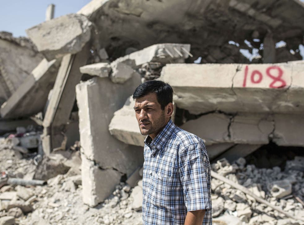 Aylan Kurdi stands in front of a neighbour's ruined home in Kobani