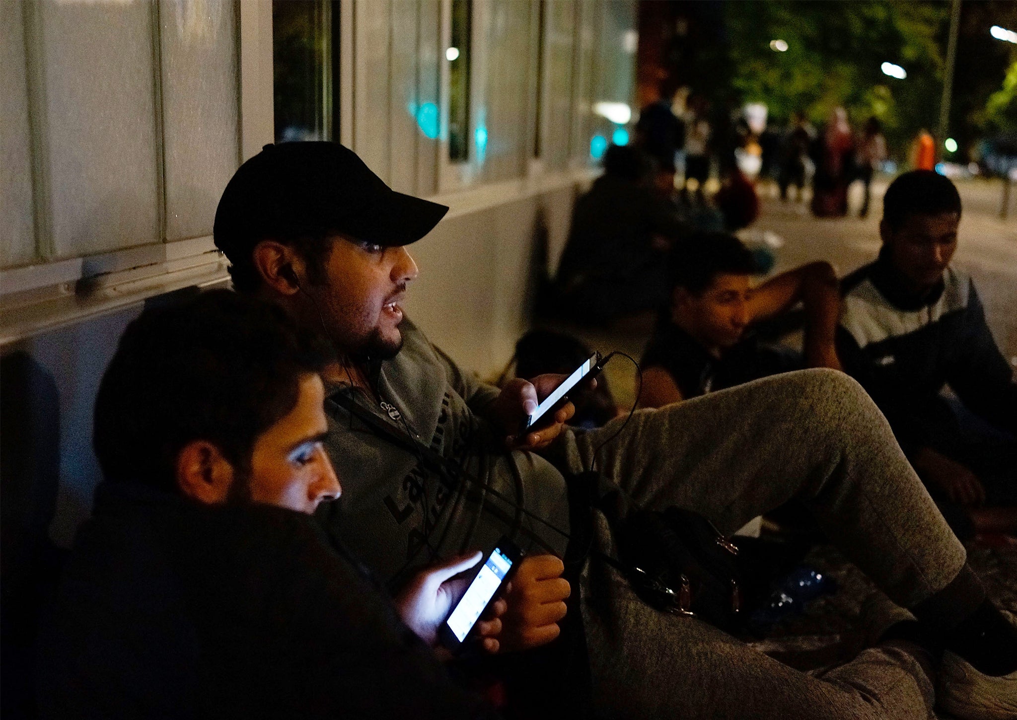 Two refugees from Syria chat on their smartphones with their relatives in Syria as they wait in front of the the Central Registration Office for Asylum Seekers in Berlin, Germany