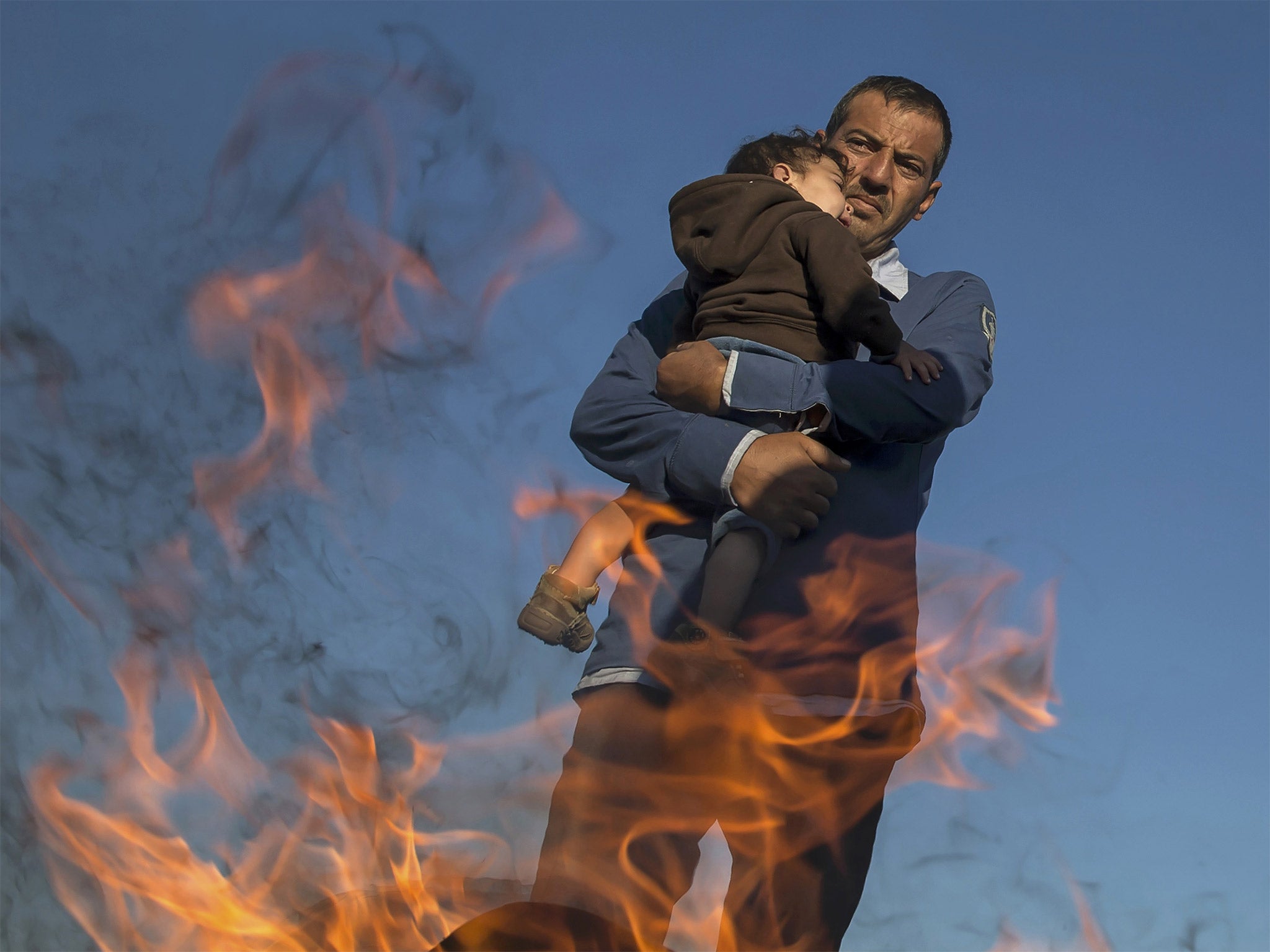 A refugee holds a child as they warm themselves by a fire in a makeshift camp at a collection point in the village of Roszke, Hungary