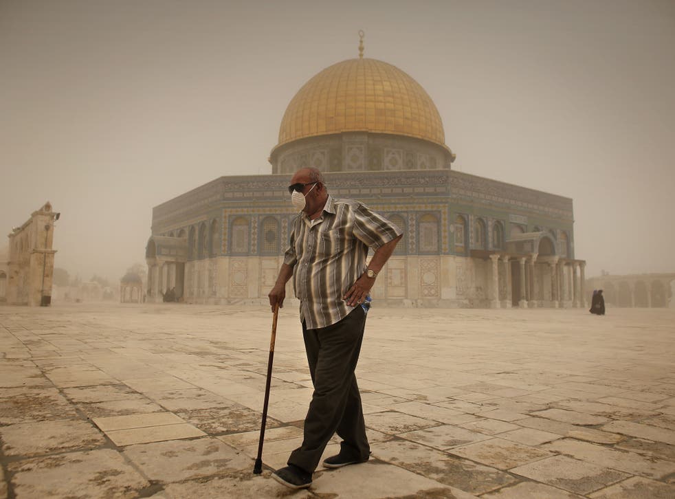 A Palestinian man wears a mask to protect his face from the dust as he walks past the Dome of the Rock mosque in the al-Aqsa Mosque compound, during a sandstorm, in the old city of Jerusalem