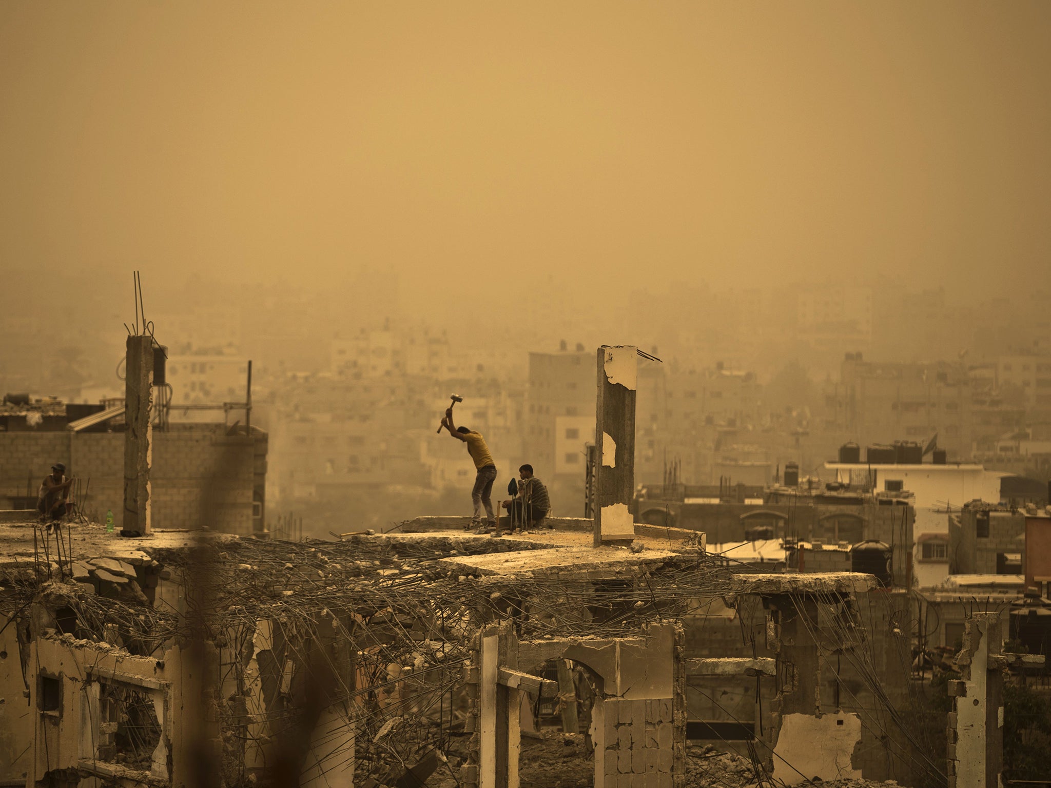 Palestinian workers remove debris from buildings, amid a sandstorm