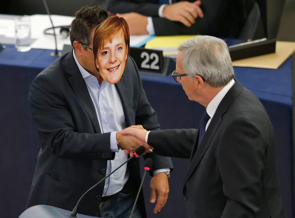 Italian Member of the European Parliament Gianluca Buonanno (L) wears a mask depicting German Chancellor Angela Merkel as he shakes hands with European Commission President Jean-Claude Juncker during his address to the European Parliament in Strasbourg