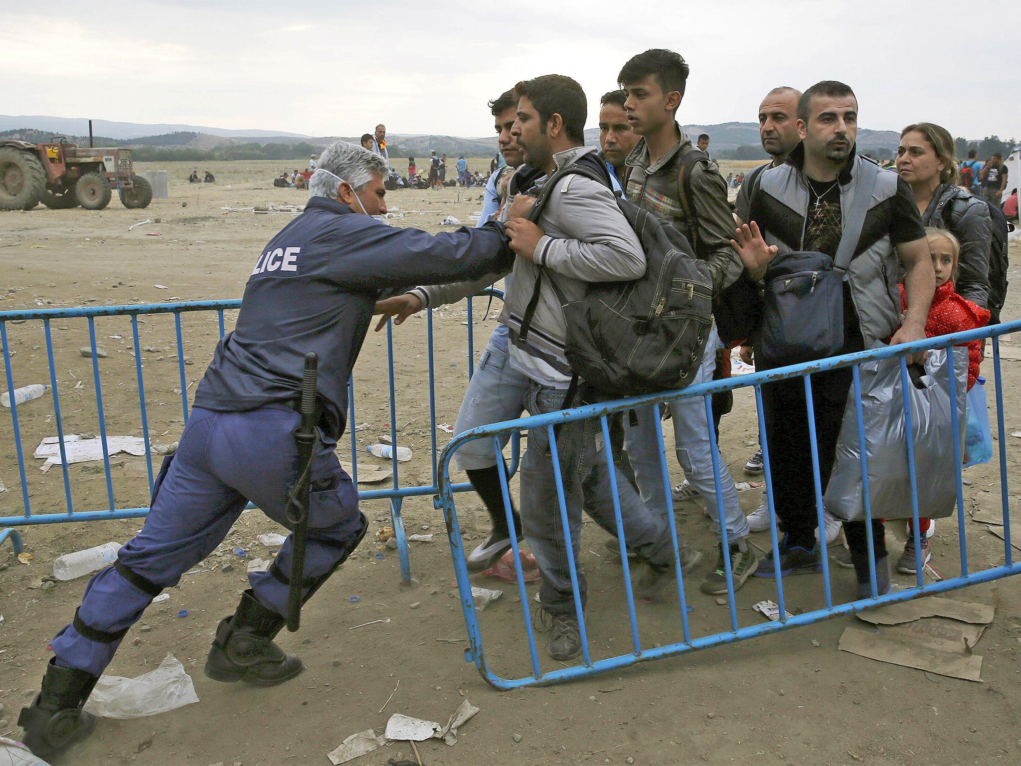 A policeman pushes refugees behind a barrier at Greece's border with Macedonia, near the village of Idomeni, Greece