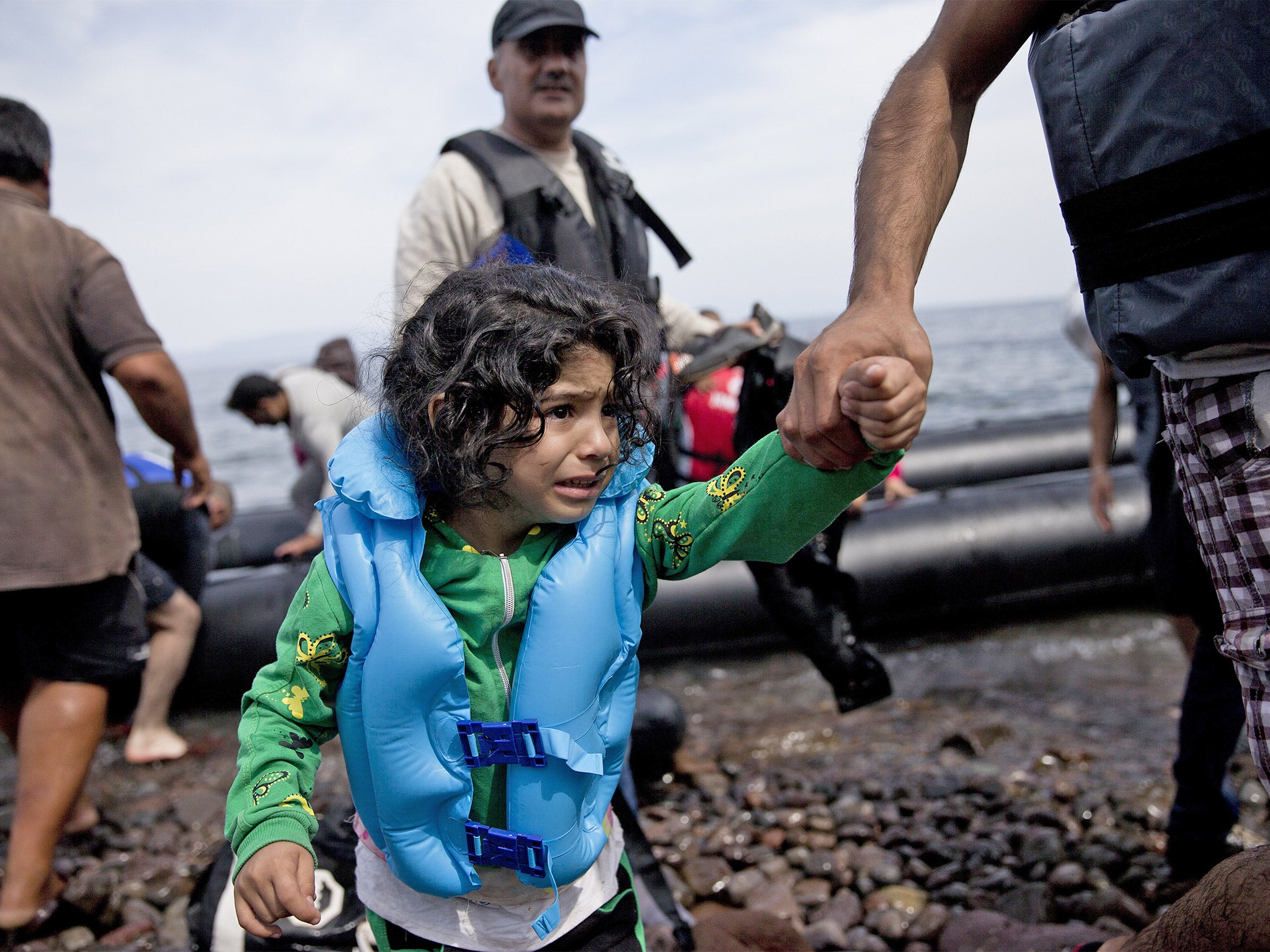 A young refugee girl is helped ashore as she arrives with others aboard a dinghy after crossing from Turkey to Lesbos island, Greece