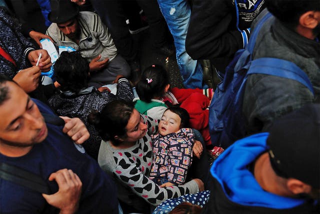 An exhausted young Syrian boy sleeps in his mother's arms as she sits on the floor in a crowd of refugees waiting to board a train bound for Munich, in Budapest