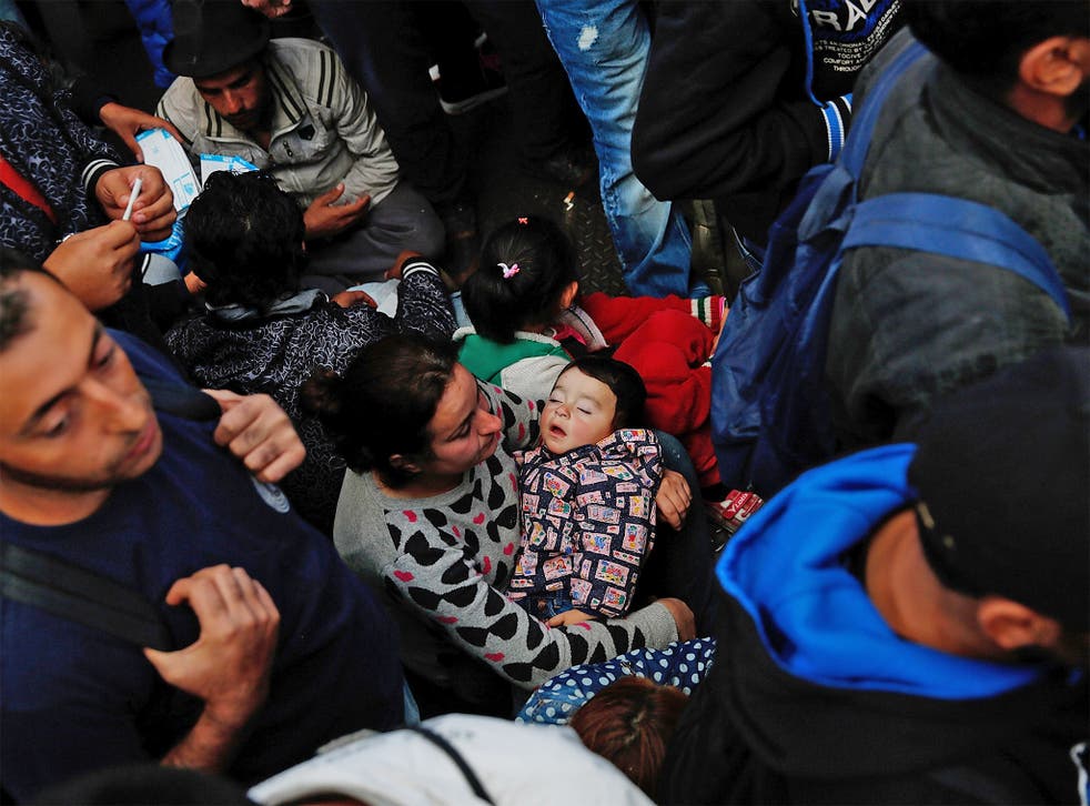 An exhausted young Syrian boy sleeps in his mother's arms as she sits on the floor in a crowd of refugees waiting to board a train bound for Munich, in Budapest