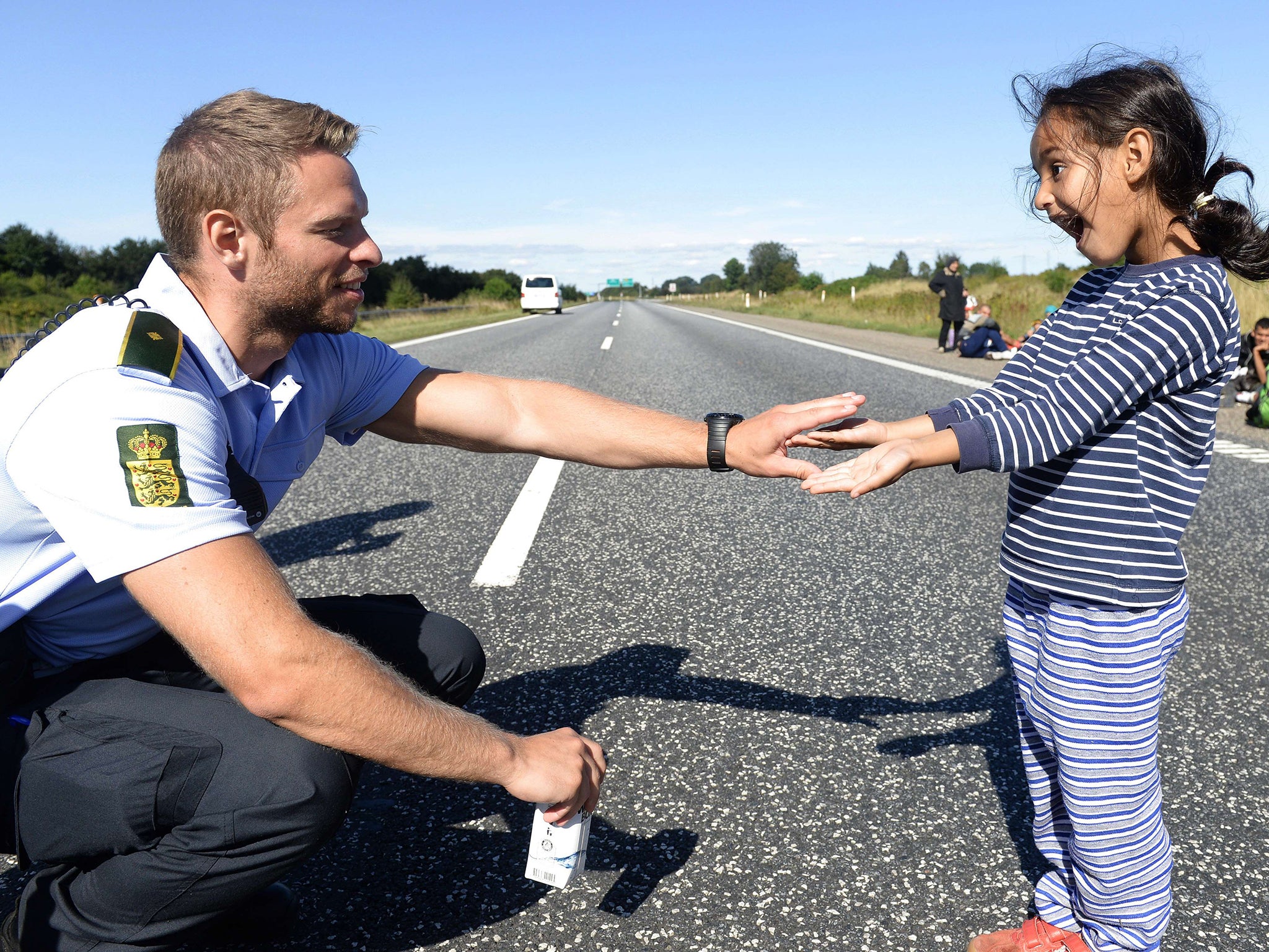 Danish policeman plays with a girl as a group of refugees attempt to walk at the E45 freeway from Padborg, on the Danish-German border, towards Sweden