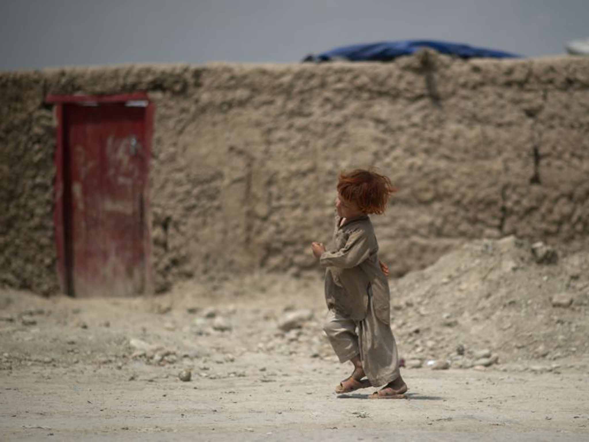 A redhead Afghan boy in Kabul, runs to a red door