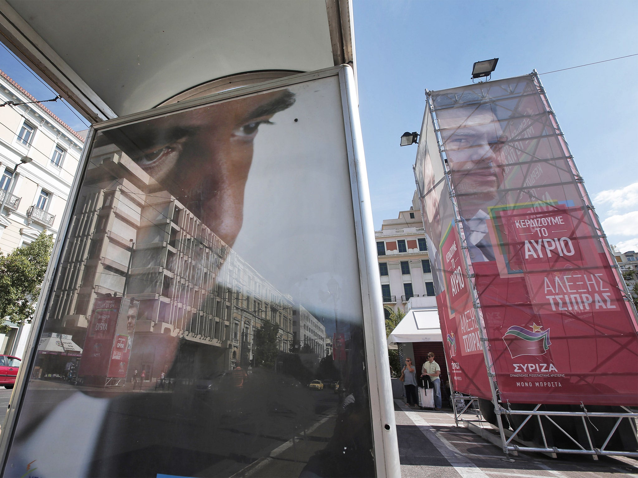 A bus stop poster depicting Vangelis Meimarakis, left, is seen backdropped by a banner, right, in support of Alexis Tsipras, in central Athens