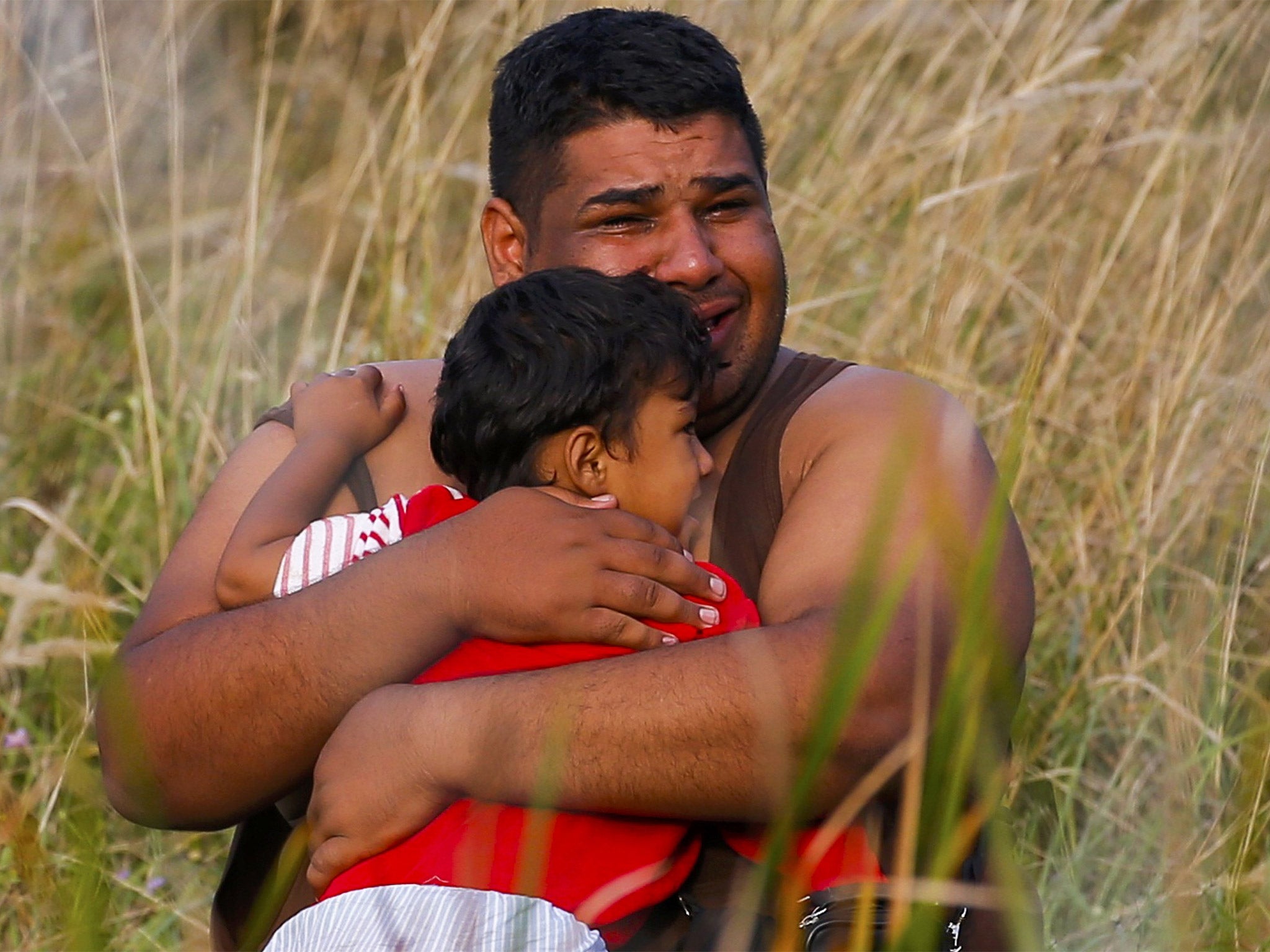 A refugee cries as he holds a child on the Serbian side of the border with Hungary in Asotthalom