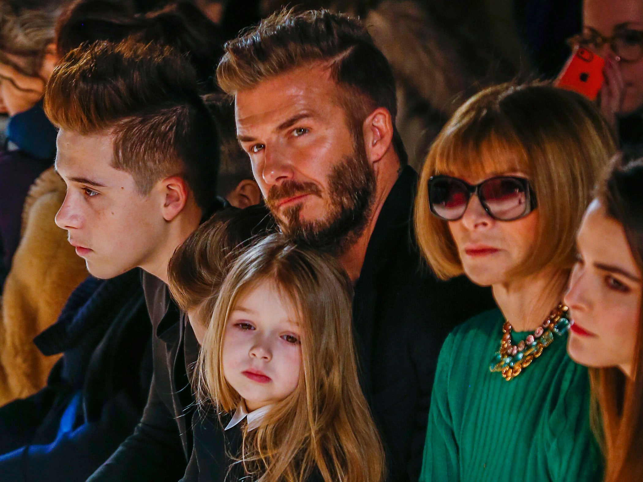 Former England captain David Beckham sits next to U.S. Vogue editor Anna Wintour (2nd R) with his daughter, Harper, on his lap and son Brooklyn (L) during a presentation of the Victoria Beckham Fall/Winter 2015 collection during New York Fashion Week Febr