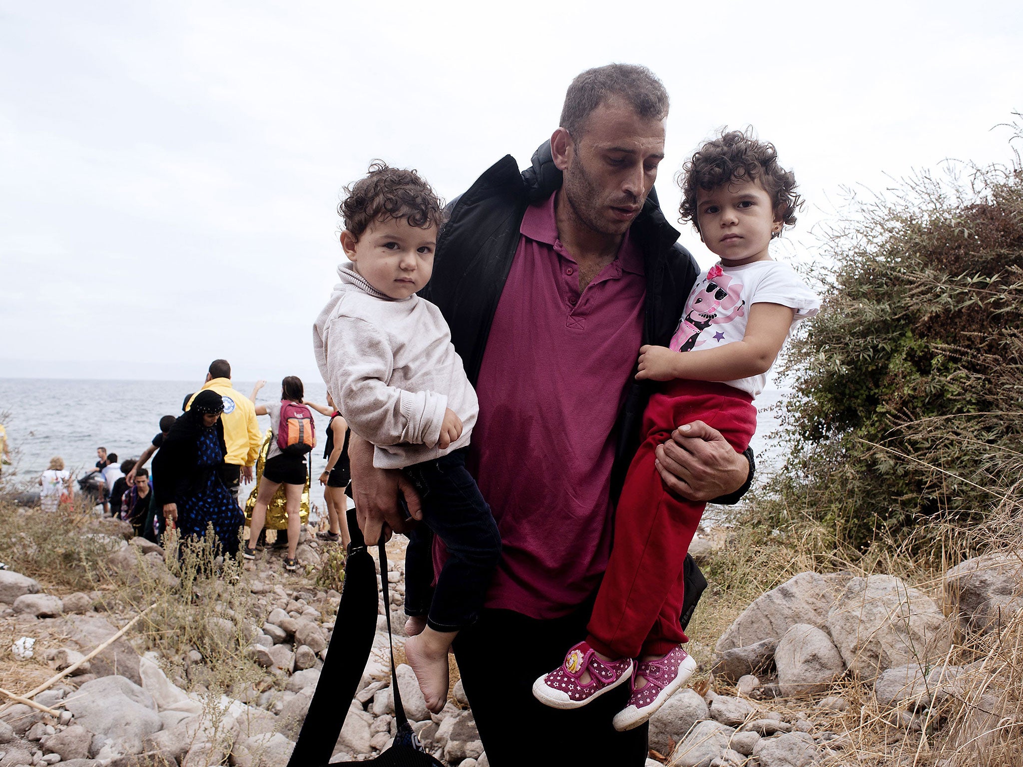A refugee carrying his children walks on Sykamia beach, west of the port of Mytilene, on the Greek island of Lesbos after crossing the Aegean sea from Turkey on September 22, 2015