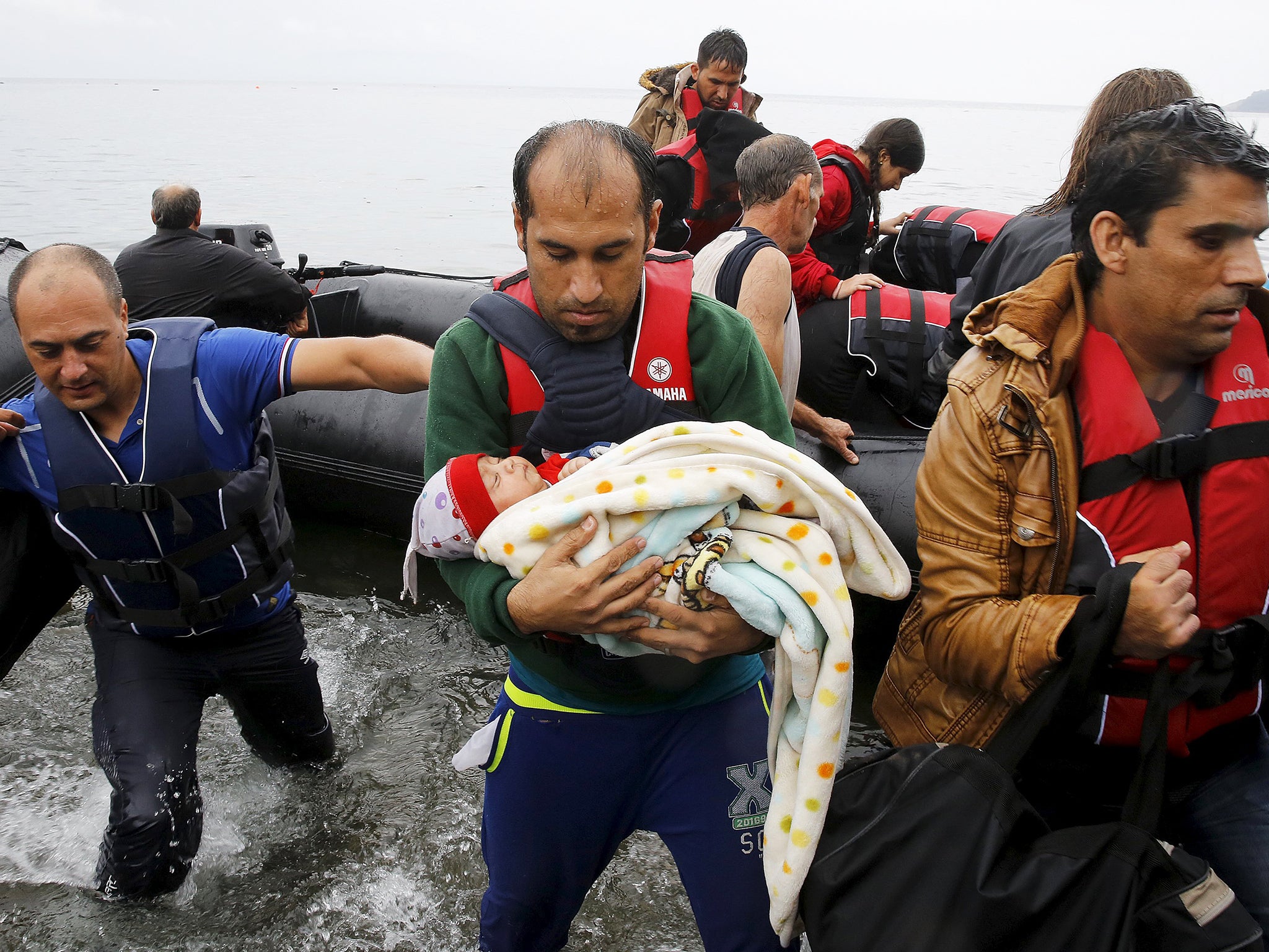 A Syrian refugee carries his baby off an overcrowded dinghy after crossing part of the Aegean Sea from Turkey to the Greek island of Lesbos