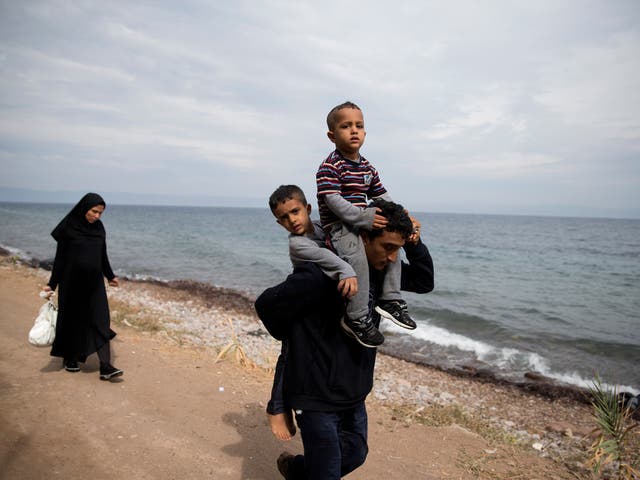 Safely ashore on Lesbos, an Afghan man carries his sons while his pregnant wife follows with their possessions