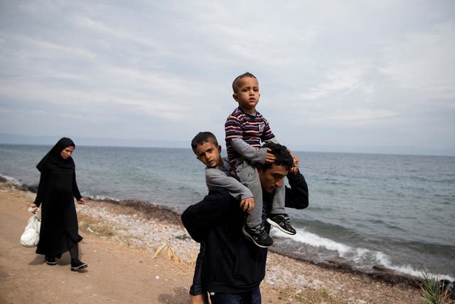Safely ashore on Lesbos, an Afghan man carries his sons while his pregnant wife follows with their possessions