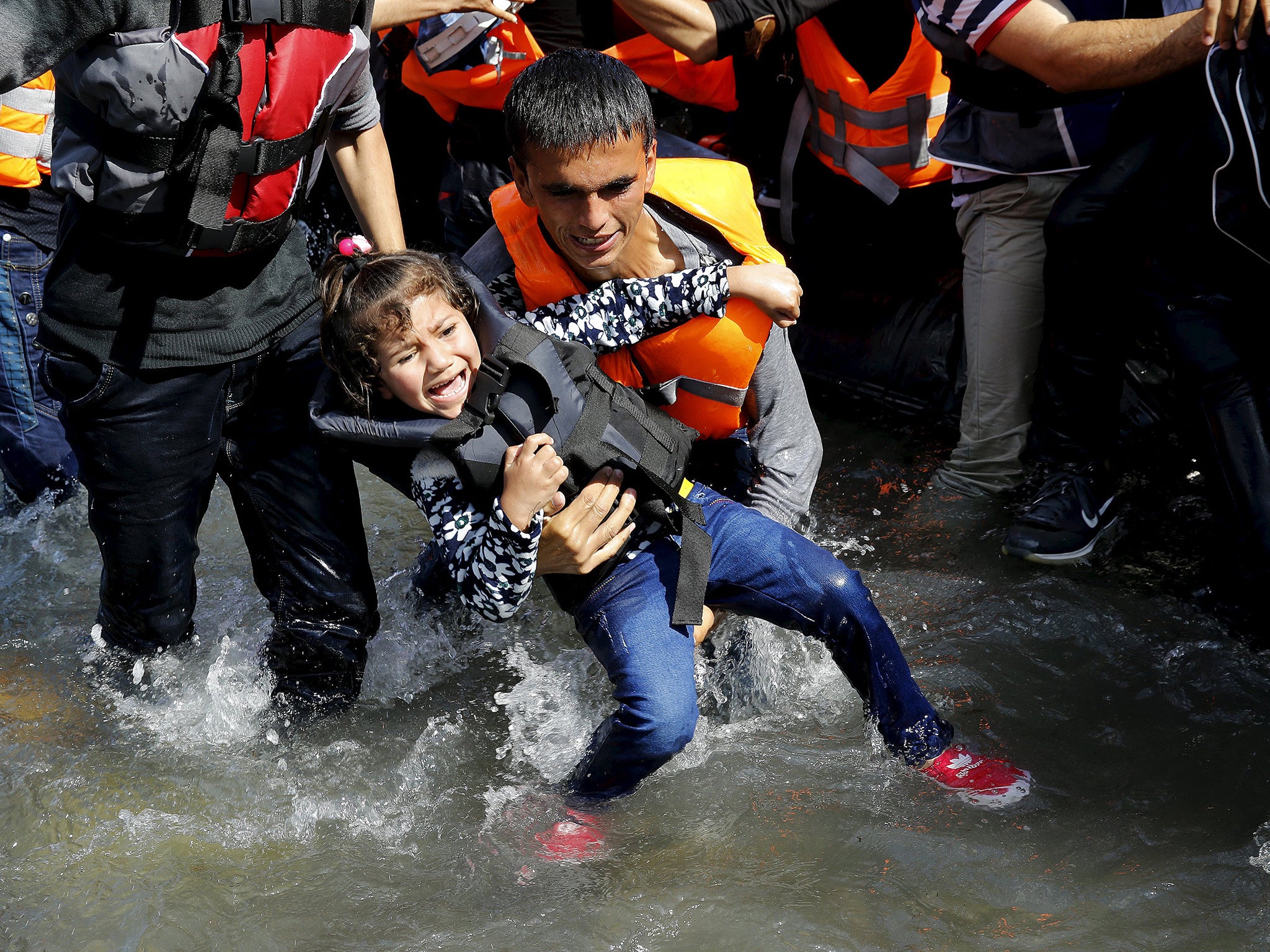 A Syrian refugee man struggles to carry his daughter off a dinghy at a beach after arriving on Lesbos