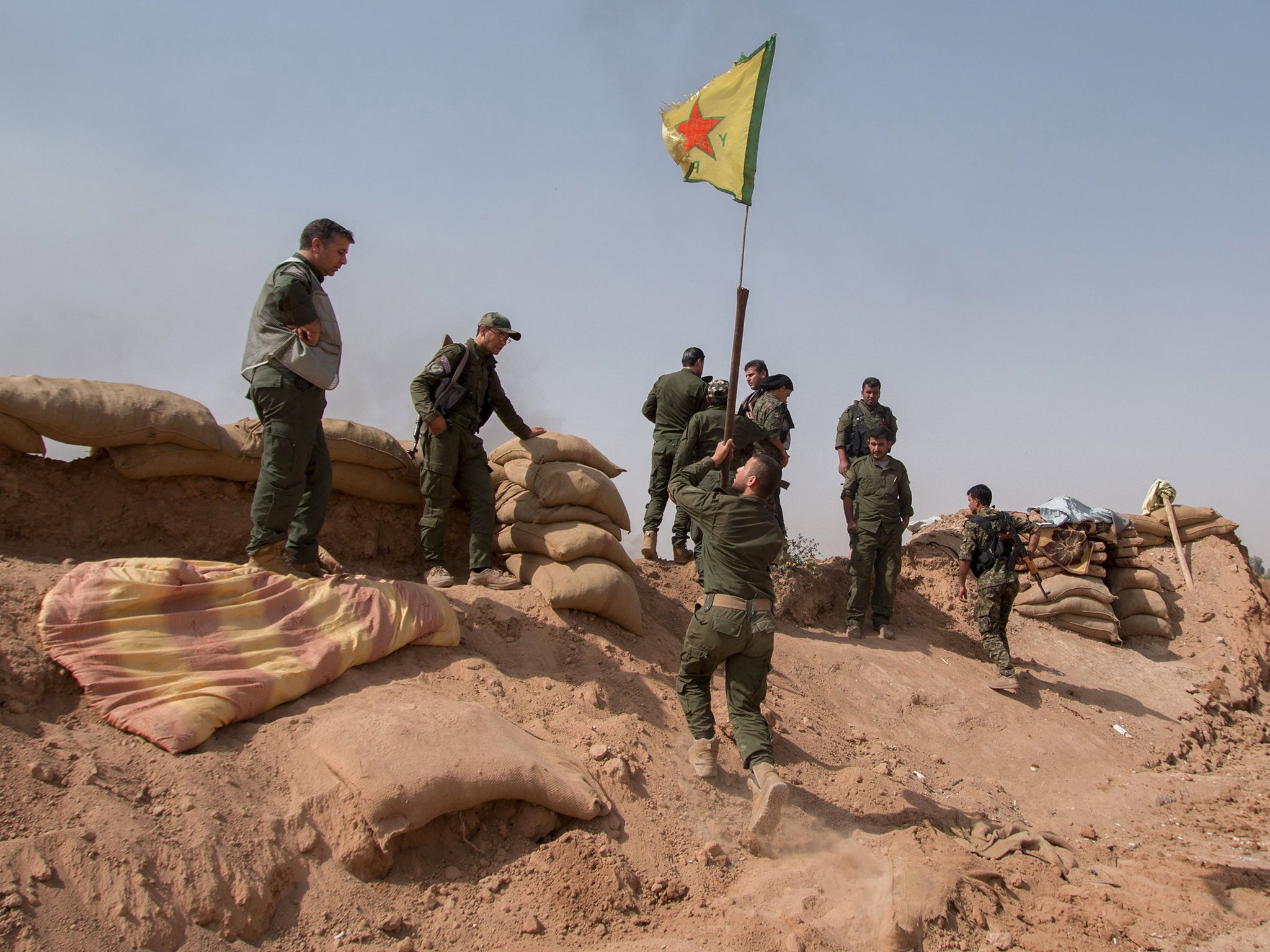 Kurdish YPG fighters raise a flag after regaining territory rrom IS outside the city of Hasaka