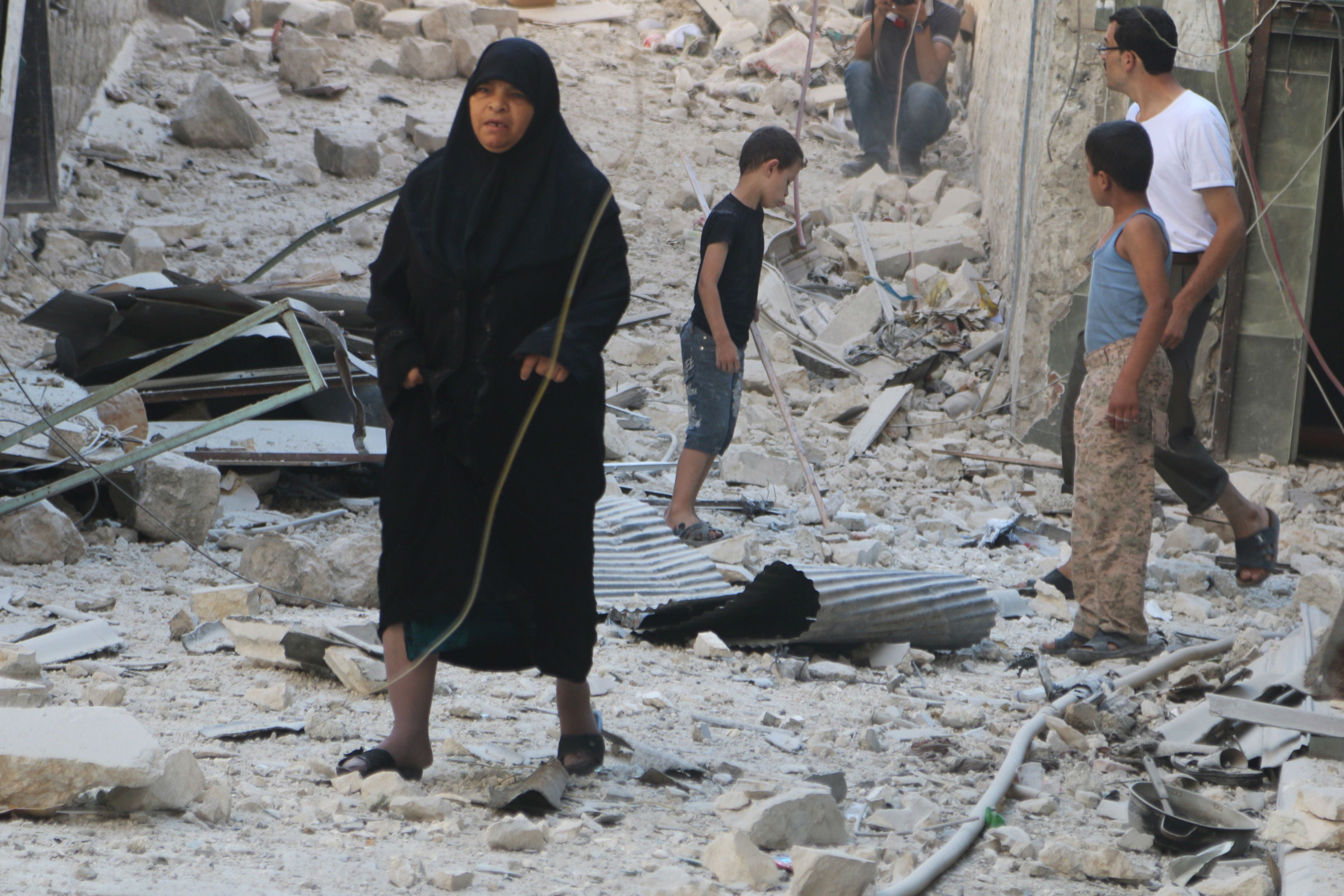 Civilians in Aleppo walk on rubble caused by barrel bomb dropped by forces loyal to President Bashar al-Assad