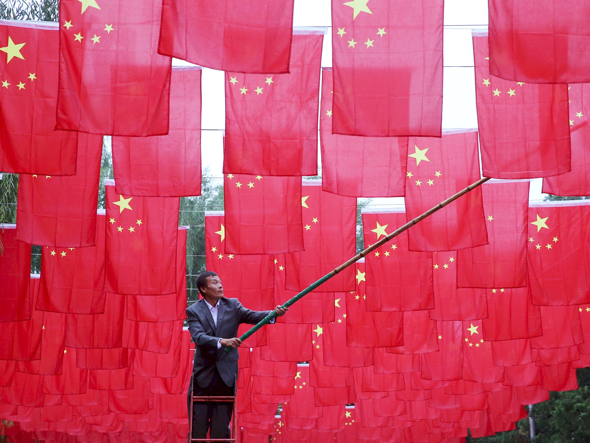 A man hangs Chinese national flags as decorations at a park, ahead of China's National Day, in Beijing