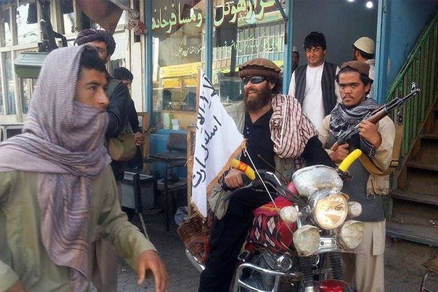 A Taliban fighter sits on a motorcycle adorned with a Taliban flag in Kunduz, Afghanistan