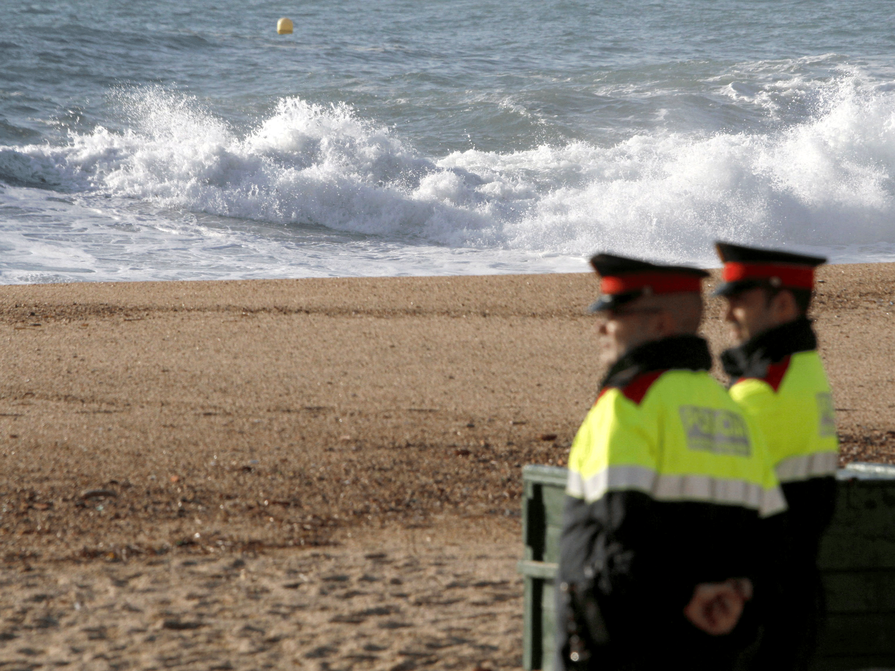 Two police officers stand on the beach of Lloret de Mar, where the drowned bodies were found