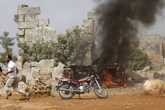 A man runs past a burning military vehicle at a base controlled by rebel fighters from the Ahrar al-Sham Movement, that was targeted by what activists said were Russian airstrikes at Hass ancient cemeteries in the southern countryside of Idlib, Syria