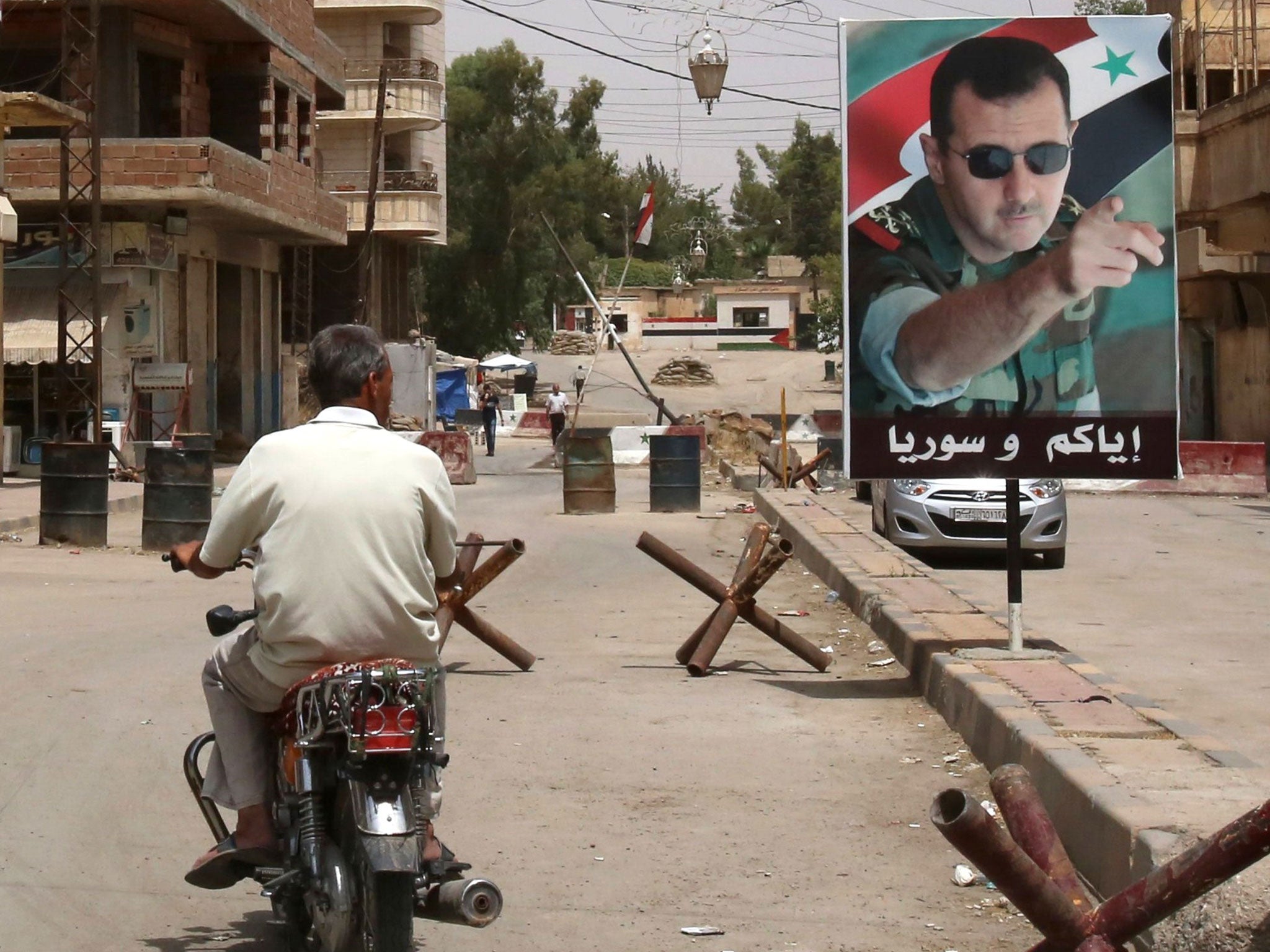 A man drives his bike past a poster of President Bashar al-Assad in the Kurdish city of Qamishli