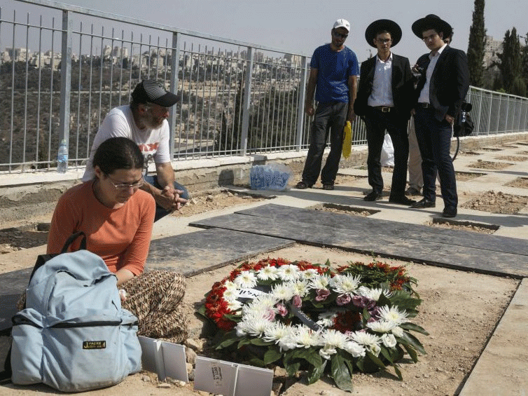 Mourners stand beside the grave of Eitam and Naama Henkin