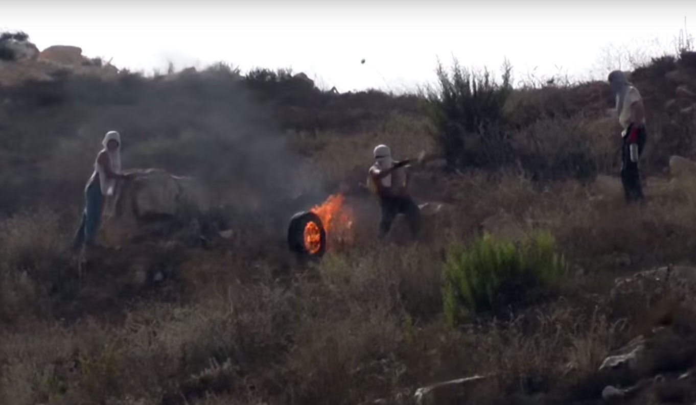 Israeli settlers roll a burning tire towards Palestinian villagers