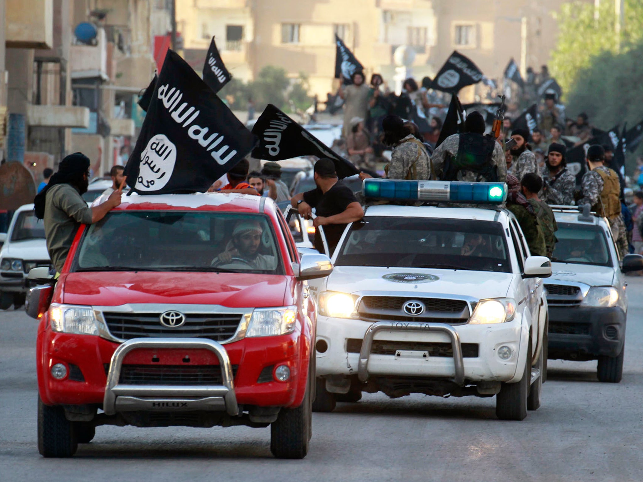 Isis fighters waving flags travel in Toyota vehicles as they take part in a military parade along the streets of Syria's northern Raqqa province