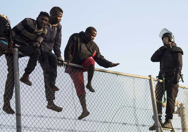 A member of the Spanish Guardia Civil sits atop a fence in Melilla, Spain, alongside would-be immigrants. Getty Images