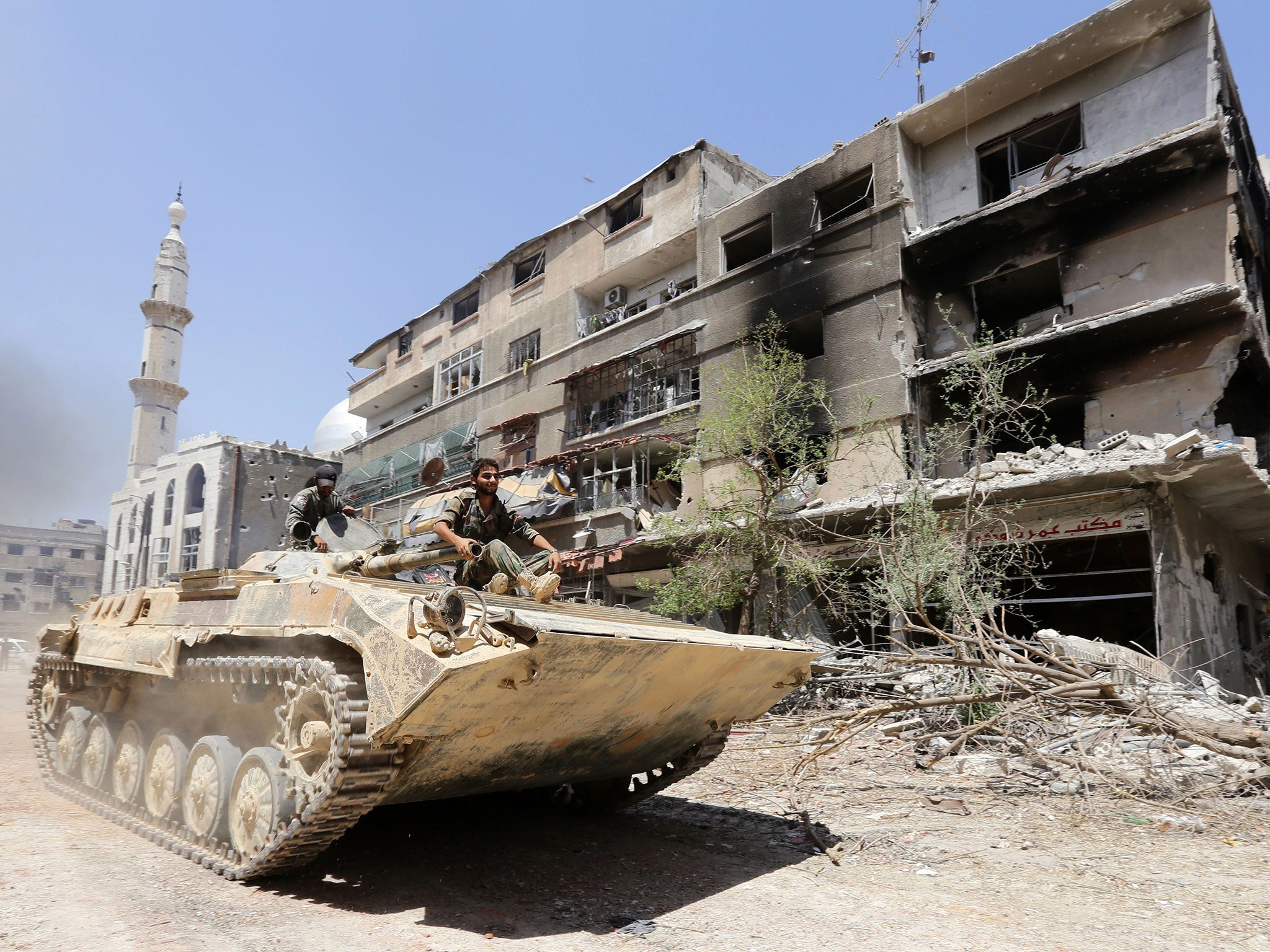 Syrian government troops sit atop a tank as they drive past a damaged building on the outskirts of the capital Damascus