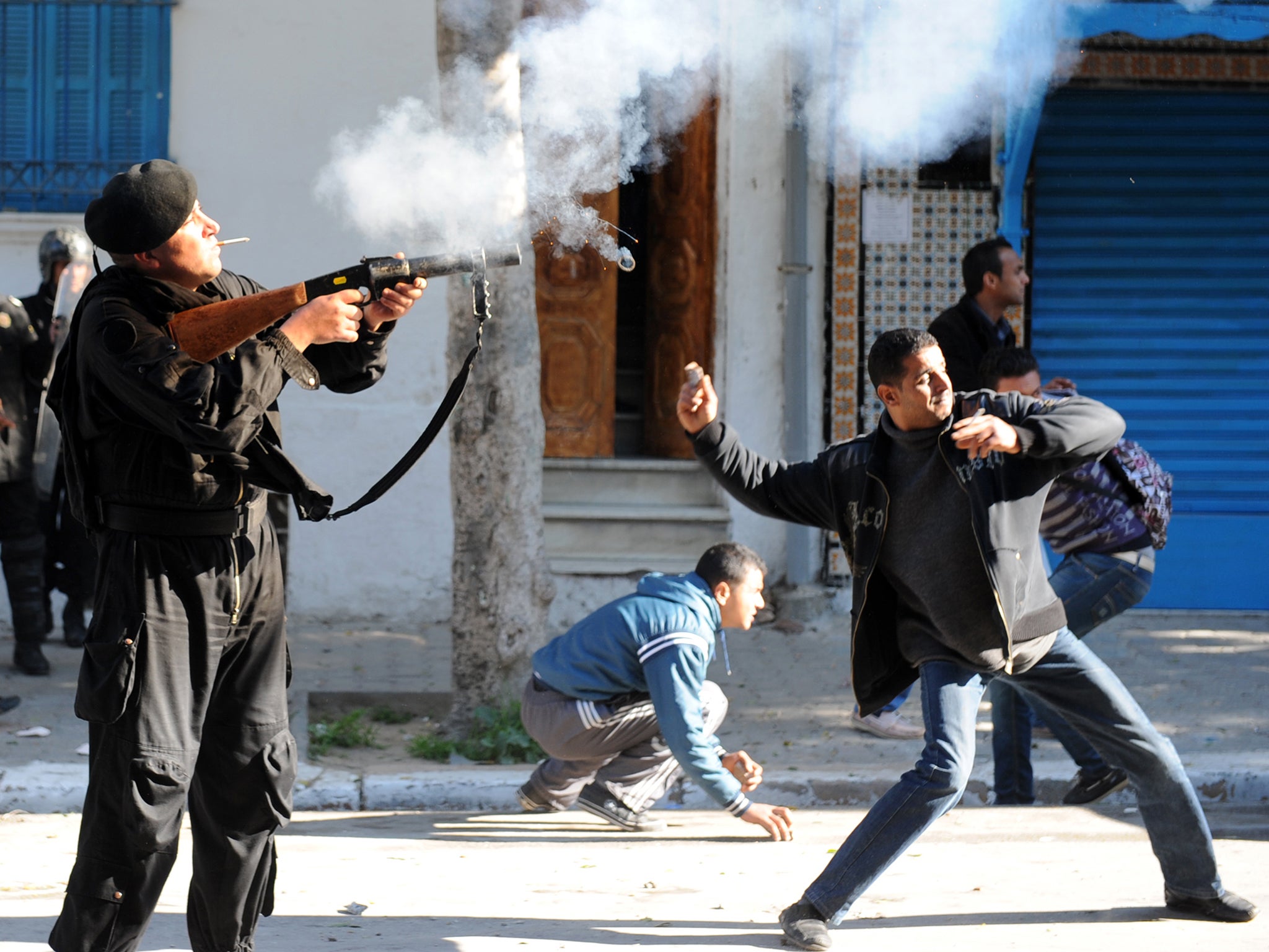A Tunis resident throws a stone while a police officer shoots tear gas canister at residents from the central Tunisian region of Sidi Bouzid on 26 January 2011 in front of Prime Minister Mohammed Ghannouchi's office in Tunis