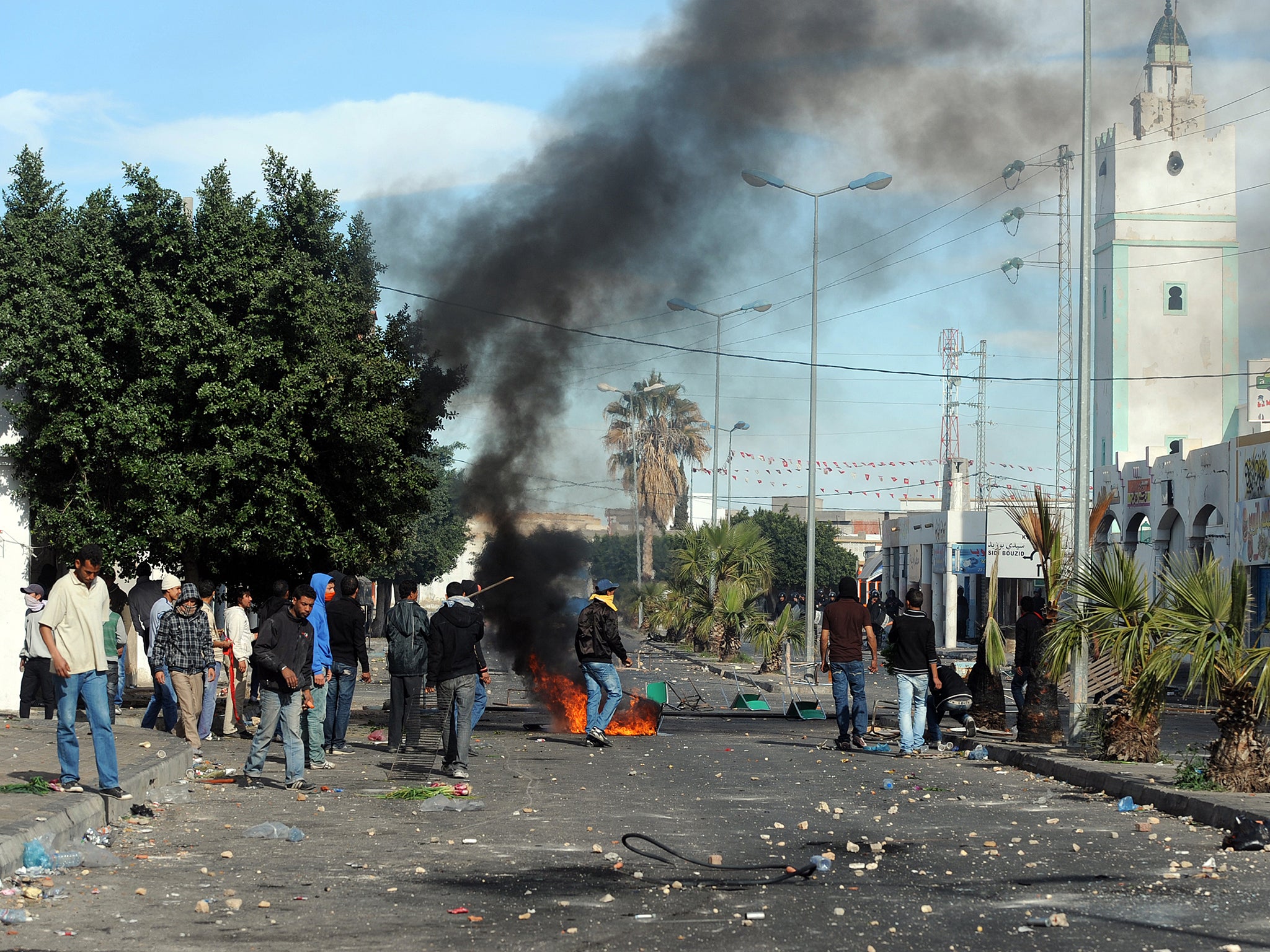 Smoke billows from an object alight as Tunisian demonstrators stand in a street during clashes with security forces on 10 January 2011 in Regueb, near Sidi Bouzid