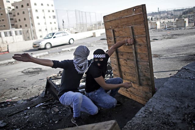 Palestinian demonstraters take shelter as they prepare to throw a molotov cocktail towards Israeli security forces