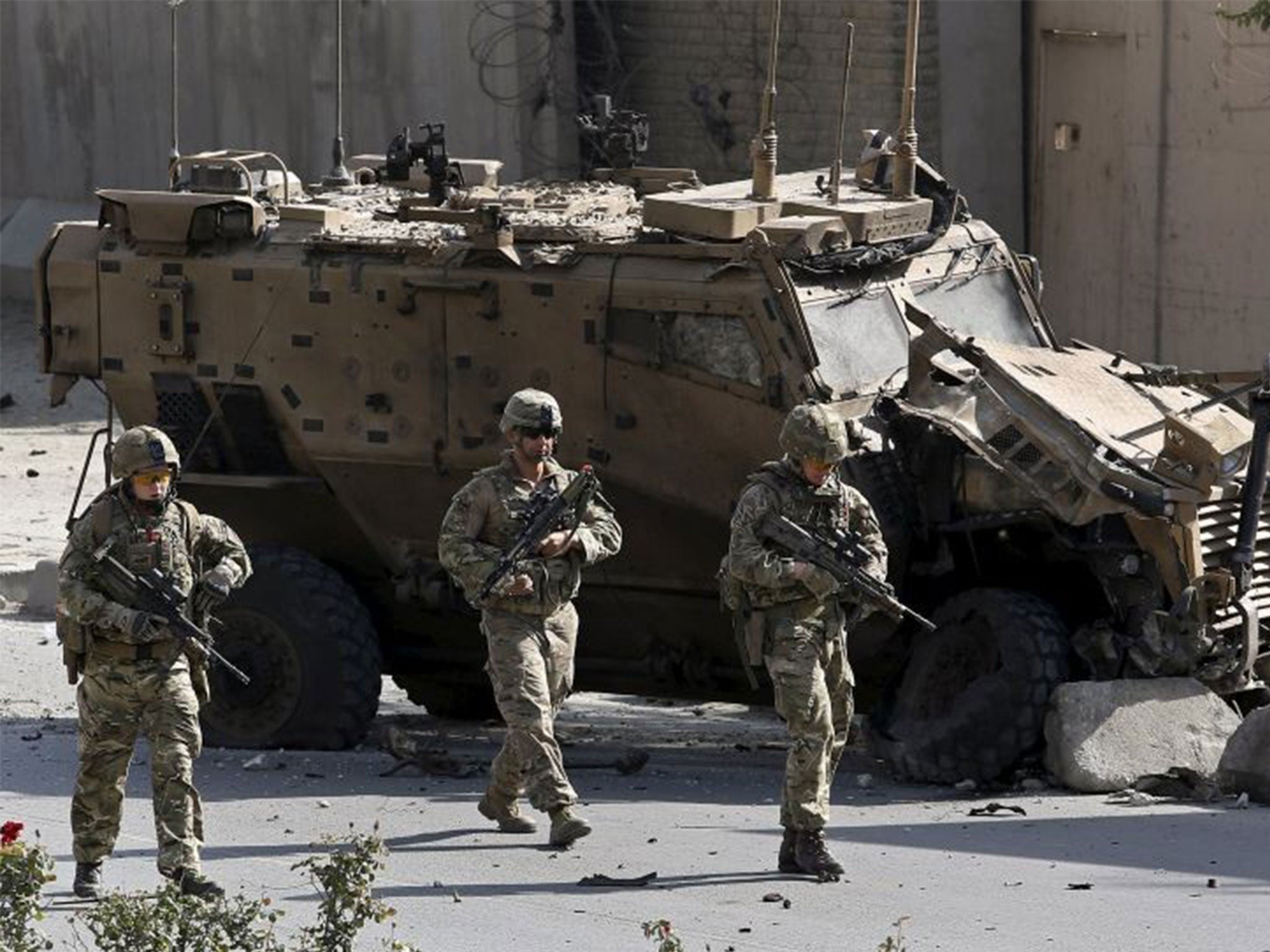 Nato soldiers walk in front of a damaged Nato military vehicle at the site of a bomb blast in Kabul